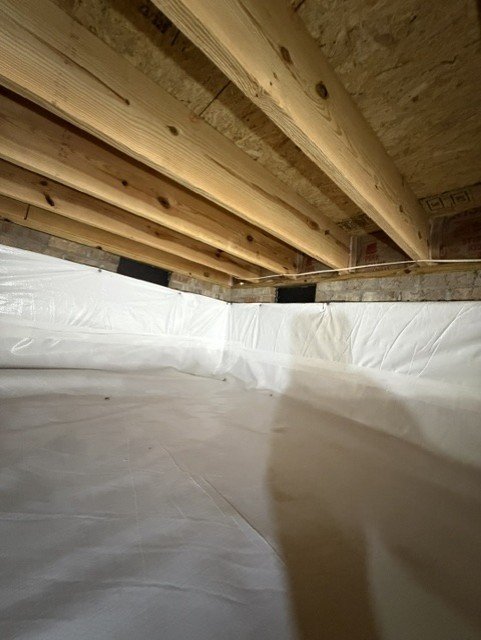 Crawlspace with white vapor barrier encapsulation and wooden floor joists