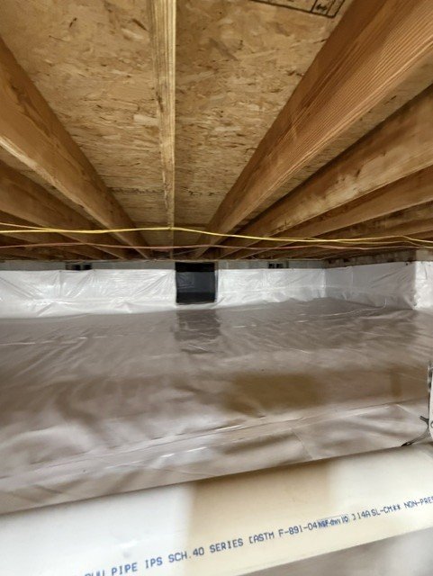 Crawlspace with white vapor barrier installed under wooden joists and beams