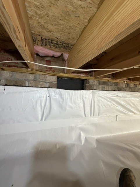 White vapor barrier installed in crawlspace with pink insulation and wooden framing visible