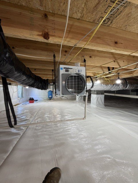 Crawlspace with white vapor barrier, dehumidifier unit, and flexible ductwork installed